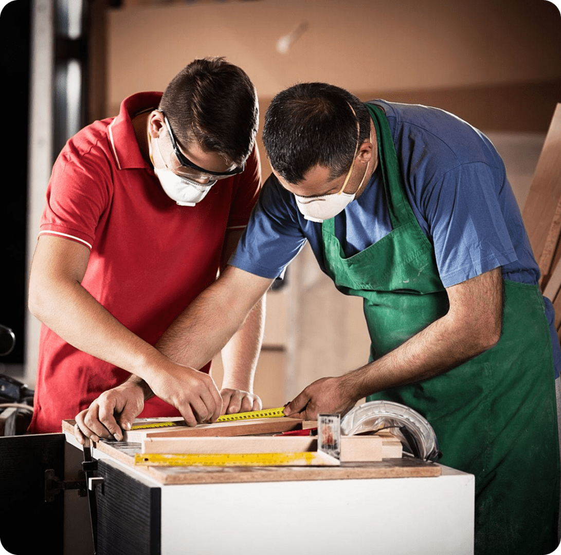 Two masked woodworkers measuring a wooden board